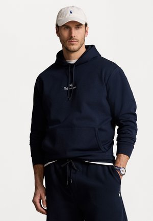 Felpa con cappuccio blu navy con cordino, ricamo del logo sul petto, tasca a kangaroo, abbinata a pantaloni della tuta coordinati e un cappello bianco.