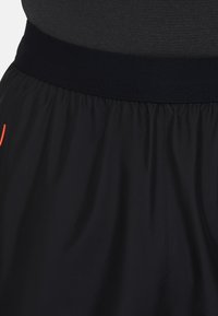 Zwarte sportshorts met een elastische tailleband, voorzien van een gladde textuur en een klein oranje accent aan de zijkant.