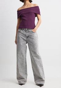 Fioletowa bluzka bez ramiączek z prążkowanej tkaniny połączona z luźnymi szarymi dżinsami. Bluzka ma falisty dekolt; dżinsy mają wypłowiały, teksturowany wykończenie.