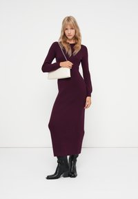 Burdeaux gestricktes Maxikleid mit langen Ärmeln und figurbetonter Silhouette. Kombiniert mit einer minimalistischen cremefarbenen Handtasche und schwarzen Stiefeletten.