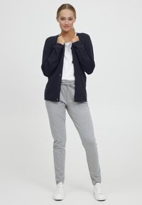 Navy textured cardigan with button accents, paired with light grey sweatpants and white sneakers. Simple, casual ensemble.
