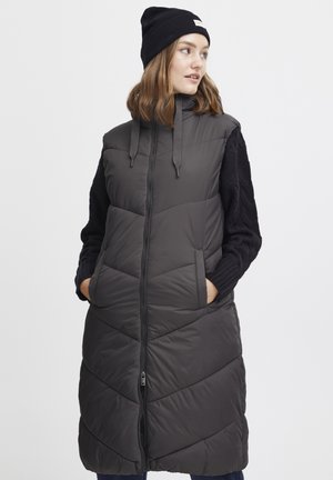 Gilet gris matelassé avec un col haut, motif en chevron, deux poches avant et manches noires tricotées. Fermeture éclair avec cordons de serrage.