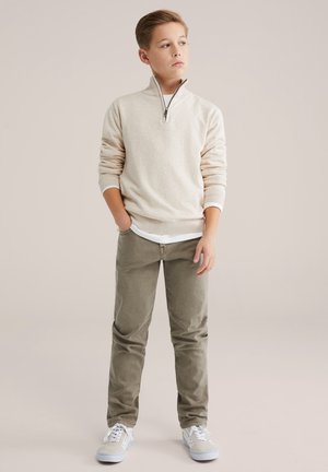 Pull beige clair à quart de fermeture éclair, couche intérieure crème, pantalon vert olive et baskets bleu clair. Textures lisses avec poignets et taille côtelés.