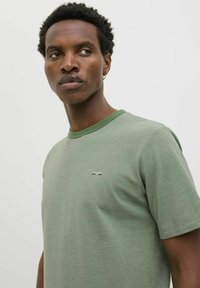 Camiseta verde de manga corta en una tela texturizada, con un cuello en verde oscuro contrastante y un pequeño logo en la parte delantera.