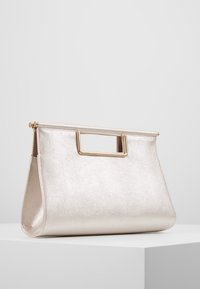 Metallinhohtoinen hopeanvärinen käsilaukku, jossa on selkeä muoto, sileä pinta ja kullanvärinen yläkahva. Varustettu vetoketjulla ja geometrisella kuviolla.