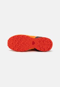 Sole di scarpa da trail running in gomma arancione e nera. Presenta una superficie testurizzata con alette multidirezionali per aderenza e trazione.