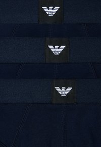 Ciemnogranatowe kąpielówki z elastycznym pasem i czarną etykietą z białym logo orła oraz kontrastującymi poziomymi paskami.