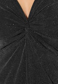 Czarny top z tkaniny z skręconym wzorem w centrum, ozdobiony rozrzuconymi srebrnymi iskrami, co dodaje tekstury i wizualnego zainteresowania.