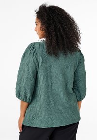 Green blouse with a textured wave pattern, 3/4 length puff sleeves, and a relaxed fit, made from a soft, lightweight fabric.