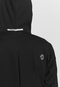 Černá kapucová bunda s matným povrchem, se subtilním logo a štítkem na zadní straně. Hladká textura a aerodynamický design.