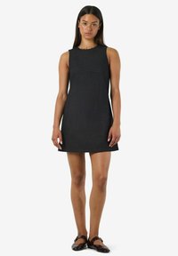 Melnas bezpiedurkņu kleitas ar pieguļošu augšdaļu un izplestu svārku, izgatavota no teksturēta auduma. Vienkāršs dizains, līdz ceļgaliem, apvienota ar tumšām kurpēm.