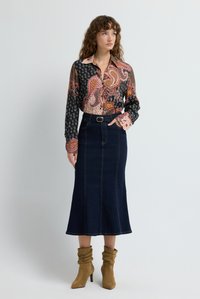 Camisa de manga larga en tejido estampado con tonos de rosa, negro y blanco; combinada con una falda midi de mezclilla oscura y botines de ante marrones.