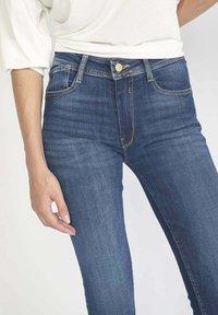 Jean bleu mi-hauteur en denim. Comprend cinq poches, des détails de couture subtils et une fermeture à bouton à l'avant.