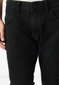 Mustmust mustreidud püksid, millel on klassikaline viie taskuga disain, nupuga lukustus ja kitsas siluett koos peente tekstuuridetailidega.