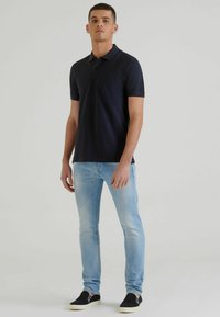 Polo shirt navy a maniche corte, con patta a due bottoni, abbinato a jeans slim-fit blu chiaro e sneakers nere senza lacci.