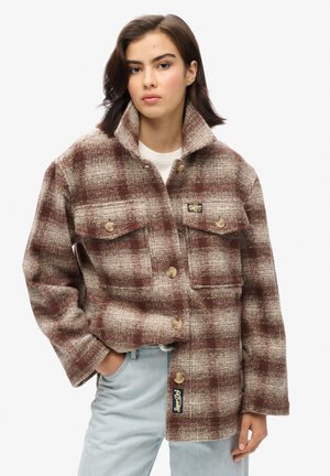 Bruine en crèmekleurige geruite jas van een gestructureerde stof, met een kraag, twee voorzakken en knoopsluitingen. Logo-opdruk aan de zijkant.