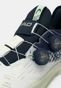 Λευκό και ναυτικό αθλητικό παπούτσι με υφή στο πάνω μέρος, σύστημα δέσης BOA και μοτίβο στη σόλα. Διαθέτει θηλιά στη φτέρνα και λεπτομέρεια πλευρικού ελέγχου.