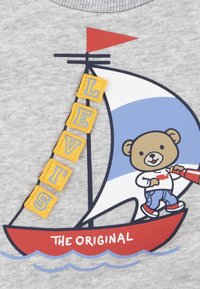 Felpa grigia con un orso su una barca, con una vela rossa. Le toppe gialle formano la scritta "LEVI'S", e "THE ORIGINAL" è stampato in rosso.
