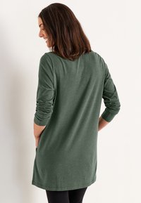Langärmliges, dunkelgrünes Tunika-Shirt aus weichem Material mit lockerer Passform, abgerundetem Saum und umgeschlagenen Ärmeln.