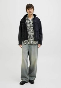 Chaqueta de mezclilla negra sobre una camisa de manga corta con estampado; jeans de pierna ancha de lavado claro; zapatos negros. Diseño simple y casual con un marcado efecto de capas.