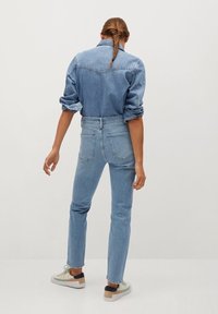 Chemise en jean bleu clair à manches longues, dotée d'un empiècement au dos et de poignets retroussés, associée à un jean taille haute bleu clair et des baskets décontractées.