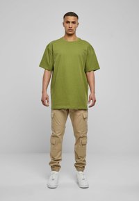 Olivegrünes, oversized T-Shirt; beiger Cargo-Hose mit mehreren Taschen; weiße Sneaker; einfaches, lässiges Design ohne Muster.