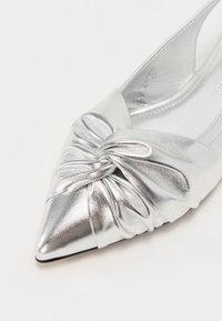 Chaussure argentée métallique à bout pointu avec un détail de tissu froncé à l'avant, texture lisse, design épuré et semelle plate.