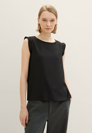 Haut sans manches en noir, texturé, avec un col rond et des détails subtils aux épaules, associé à un pantalon gris. Un design simple et moderne.