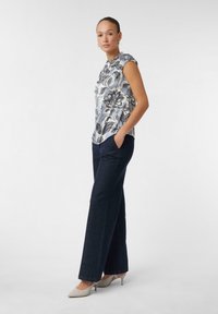 Hellbluse mit floralen Mustern und kurzen Ärmeln, kombiniert mit weiteren dunkelblauen Denim-Hosen und beigen Slingback-Heels, vor einem weißen Hintergrund.