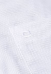 Weißer, texturierter Stoff mit einem Diamantmuster. Auf der Oberfläche befindet sich ein kleines gesticktes Logo in einem quadratischen Rahmen.