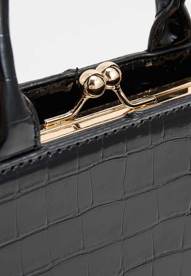 Sac à main noir en simili-cuir crocodile avec une finition brillante, doté d'une fermeture à verrou tournant dorée et de deux poignées. Forme rectangulaire compacte.