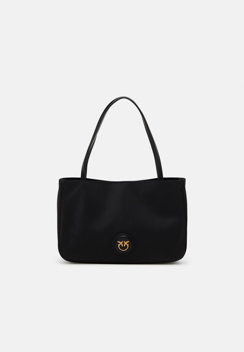 Sac à main noir porté à l'épaule avec deux anses et un petit logo doré circulaire au centre devant.