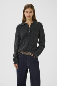 Pull en tricot gris foncé avec un col et une patte de boutonnage. Porté avec un jean bleu foncé et une ceinture marron. Texture douce, coupe décontractée.