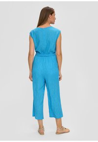 Un catsuit blu a maniche corte con vita con cinturino, pantaloni a 3/4 e un tessuto texturizzato. Design semplice senza fantasie o decorazioni.