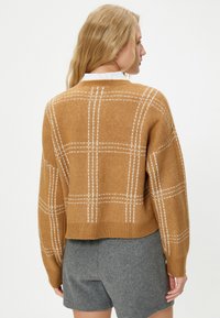 Braun karierter Pullover mit einem cropped Design, gestrickter Textur, weißem Karomuster und geripptem Saum, kombiniert mit grauen Shorts.