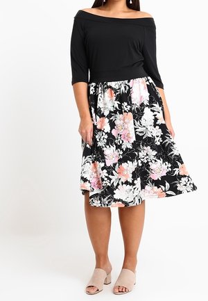 Black, off-the-shoulder top paired with a floral skirt featuring pink and white flowers on a black background. Tan block-heeled shoes.