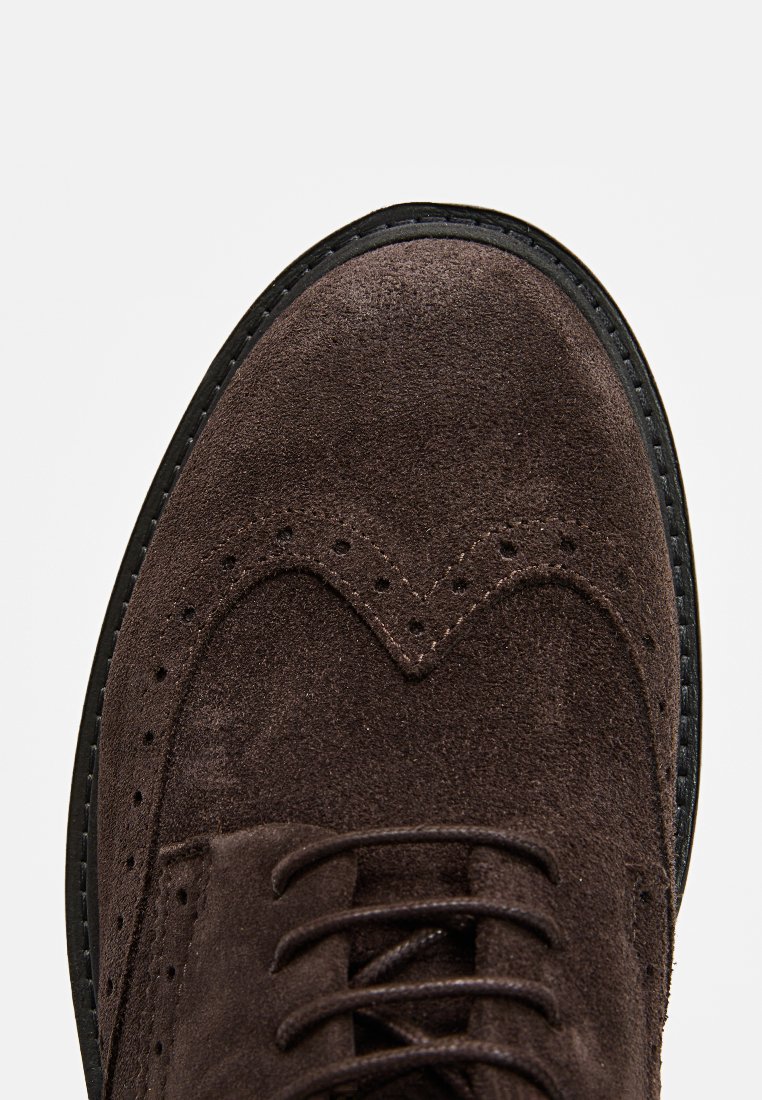 Brązowe zamszowe buty typu wingtip z czarnym przeszytym brzegiem i perforacjami brogue, z zaokrąglonym noskiem i dopasowanymi brązowymi sznurowadłami.