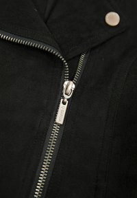 Giacca in suede nera con zip argentata e dettagli con bottone a scatto, dotata di colletto classico e finitura testurizzata. La zip è fornita di etichetta.