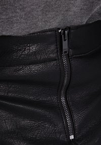Zwarte faux leren rok met een zichtbare ritsdetail. Textuur oppervlak met een lichte glans. Bovenste deel heeft een grijze stofafwerking.