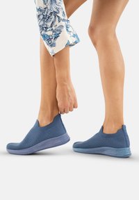Zapatillas azul de tipo slip-on con parte superior de punto texturizado y suela de degradado suave. El diseño presenta un corte bajo y tobillo elástico para facilitar su uso.
