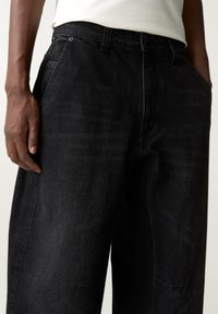 Pantalones vaqueros negros con corte de pierna recta, que cuentan con un diseño de cinco bolsillos, cierre de botón y cremallera, y detalles de costuras limpias y minimalistas.