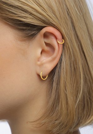Goldene Creolen mit einer glatten, polierten Oberfläche; ein Ohrstecker hat ein Hufeisen-Design, der andere ist ein kleiner, zarter Cuff.