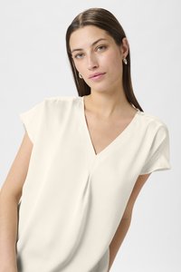 Short-sleeved, V-neck blouse in cream with a textured fabric. Features subtle draping and a loose fit, accentuating a relaxed silhouette.