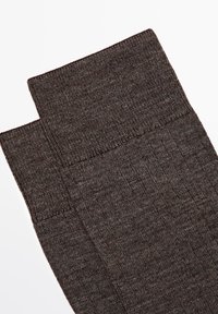 Brune ribbede knæhøje sokker lavet af et blødt materiale, der har en glat topkant og en tekstureret krop med et subtilt mønster.