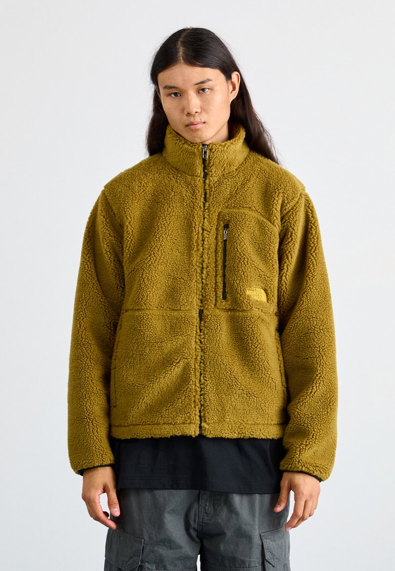 Veste en polaire de couleur vert olive avec fermeture éclair intégrale, col haut et poche poitrine zippée. Tissu texturé et doux, coupe décontractée.