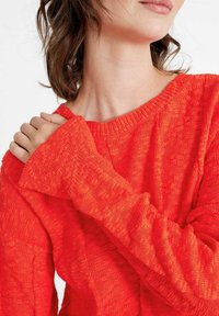 Maglione lavorato a maglia rosso con scollatura ampia e maniche lunghe. Il tessuto appare morbido con una vestibilità ampia e dettagli di cucitura visibili.