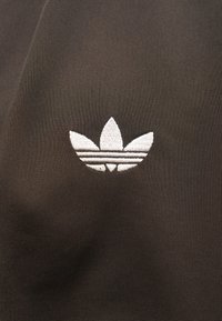 Μαύρο ύφασμα με λευκό κεντημένο λογότυπο που απεικονίζει τρία σχήματα που μοιάζουν με φύλλα και οριζόντιες ρίγες στη βάση.