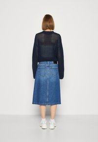 Suéter de punto azul marino con un corte holgado, combinado con una falda de mezclilla hasta las rodillas que presenta dos bolsillos traseros y una textura suave.