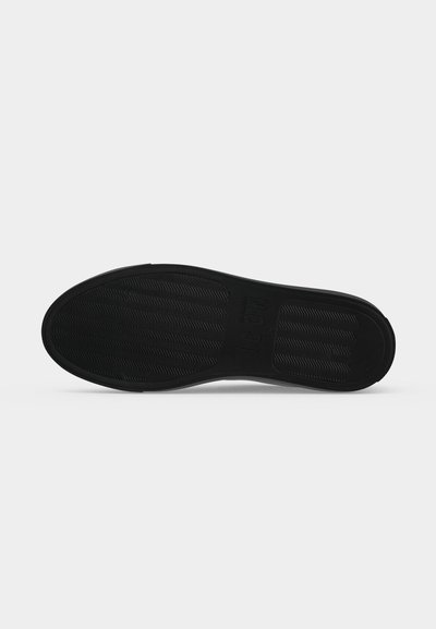 Semelle de chaussure noire avec des motifs de grip texturés et le mot "NOCT" embossé dans la partie centrale sur un fond uni.