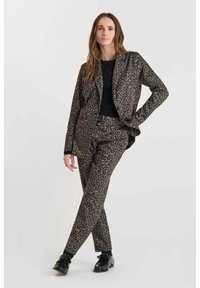 Un costume à imprimé léopard en tissu avec une texture lisse. Comprend une veste à col en pointe et un pantalon ajusté. Des chaussures noires complètent le look.